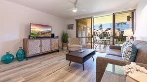 Un salon moderne avec un canapé, une table basse et un téléviseur posé sur un meuble. Une porte-fenêtre coulissante donne accès à un espace extérieur aménagé avec une table et des chaises de patio.
