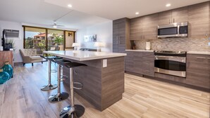 Une cuisine moderne dotée d’un îlot central, d’appareils électroménagers en acier inoxydable et offrant une vue sur l’extérieur.