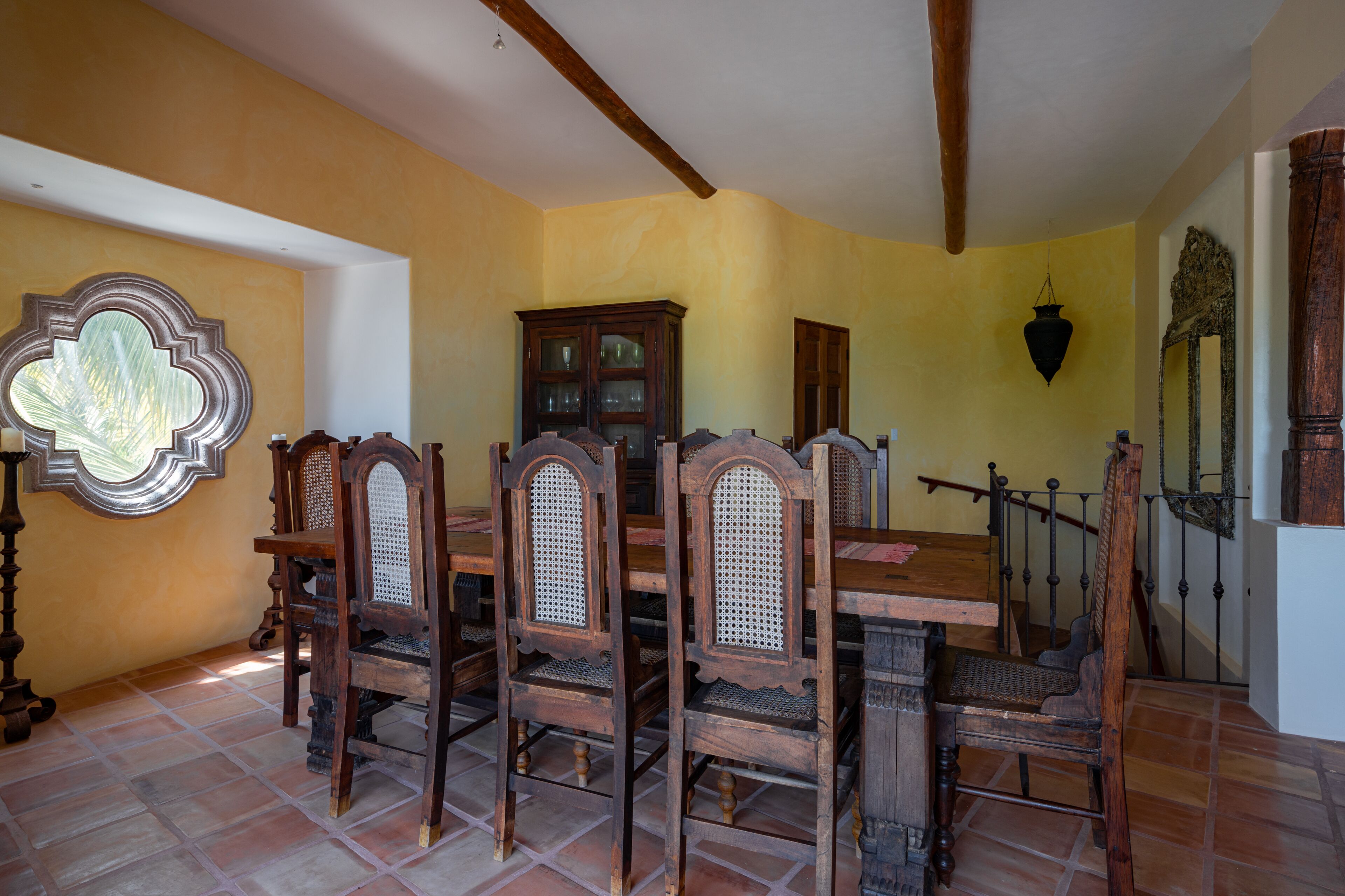 Een eetruimte met een houten tafel en stoelen, een grote kast en een decoratieve spiegel.