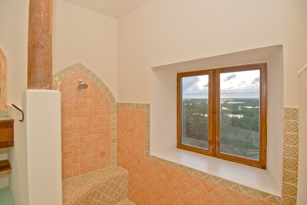 Une salle de bain avec un sol carrelé, une fenêtre donnant sur un beau paysage et une colonne en bois.