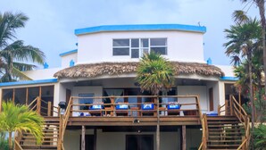 A two-story building with a thatched roof, wooden balconies, and a sandy ground. - San Pedro 5-bedroom, 4-bathroom Villa Pearl, ocean views, concierge onsite (San Pedro)