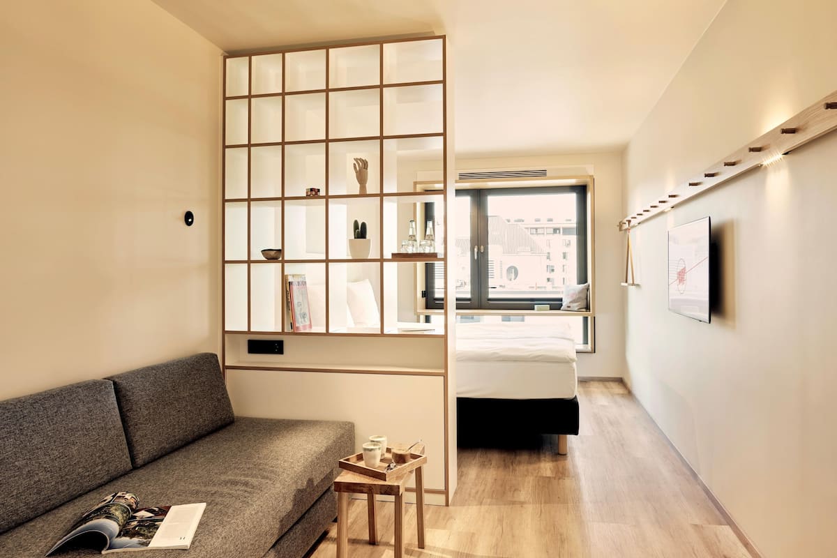 A compact living space with a sofa, a built-in bookshelf, a window with a view, and a mounted TV.