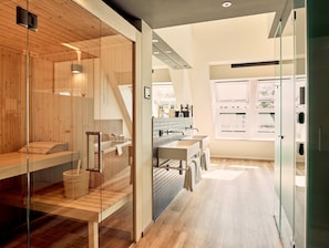 A modern bathroom with a glass shower enclosure, wooden flooring, and a visible kitchen area with a window. - Schwabinger Wahrheit by Geisel (Munich)