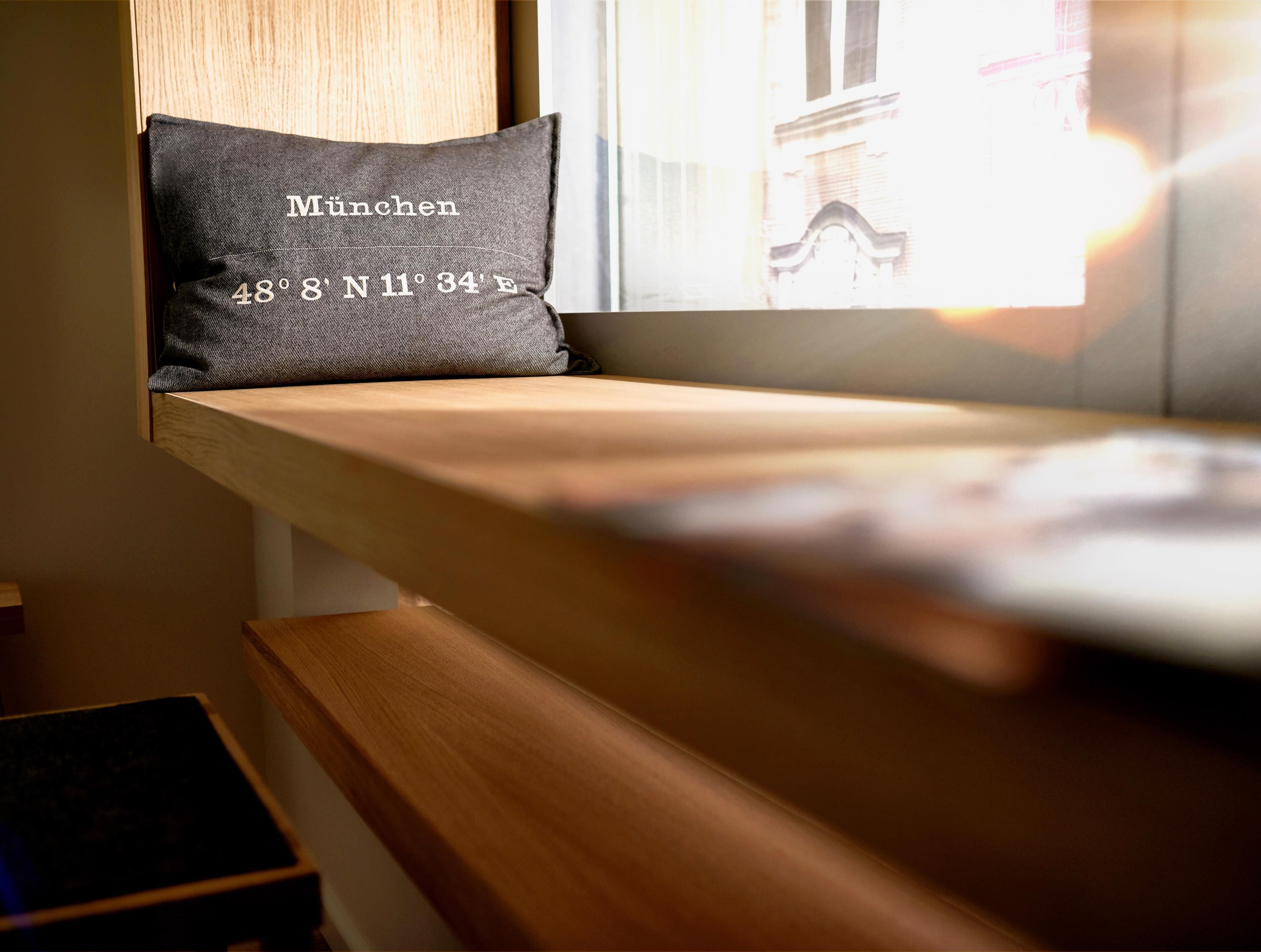 A window seat with a cushion labeled 'München 48° 8' N 11° 34' E'.