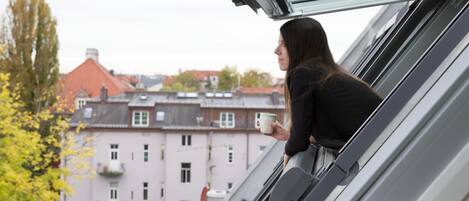 A person leaning out of a window with a cup, overlooking a building with multiple windows and balconies.