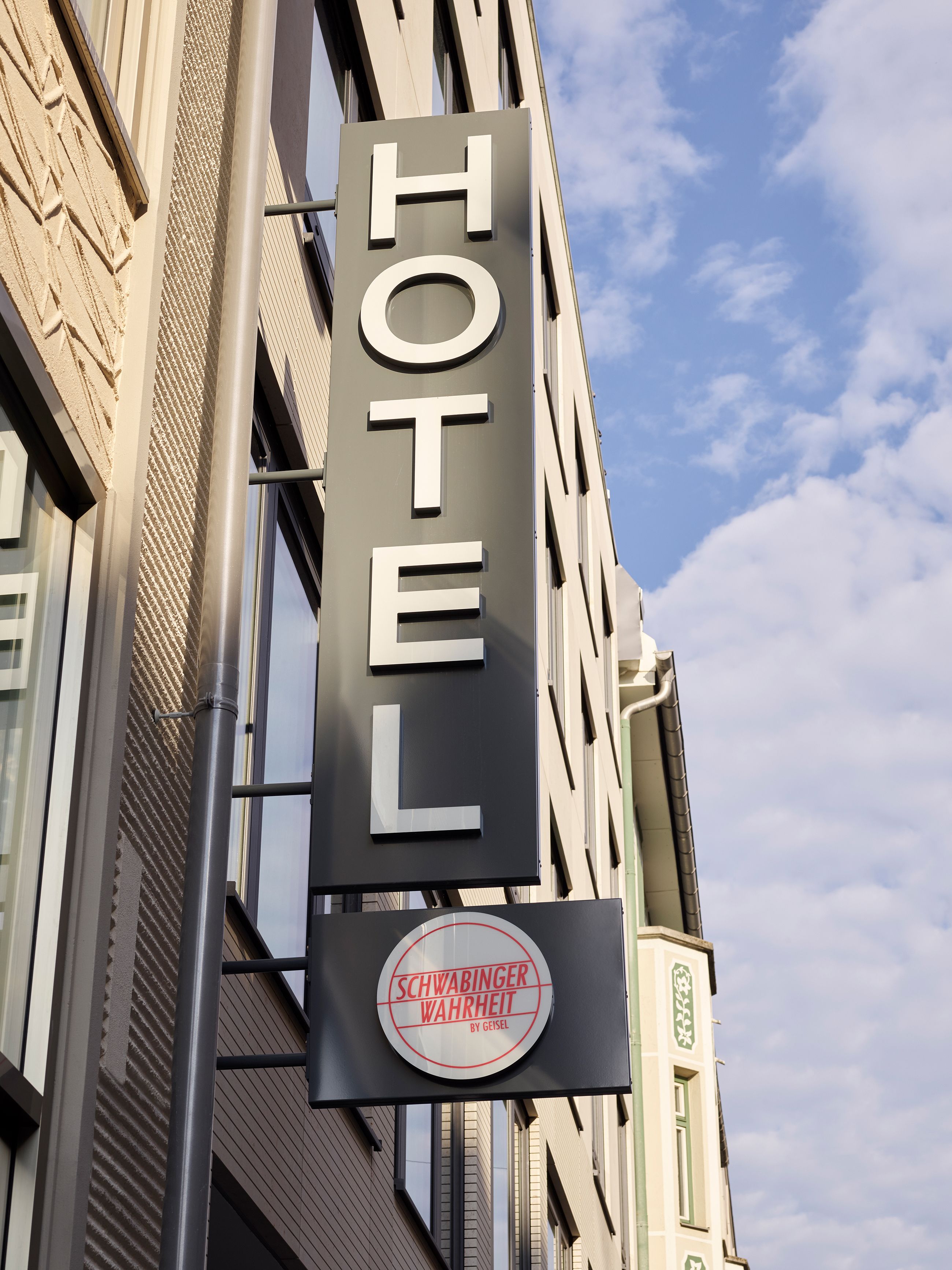 A hotel sign with the name "HOTEL" and a circular sign below it that reads "SCHWABINGER WAHREIT BY GEISEL".