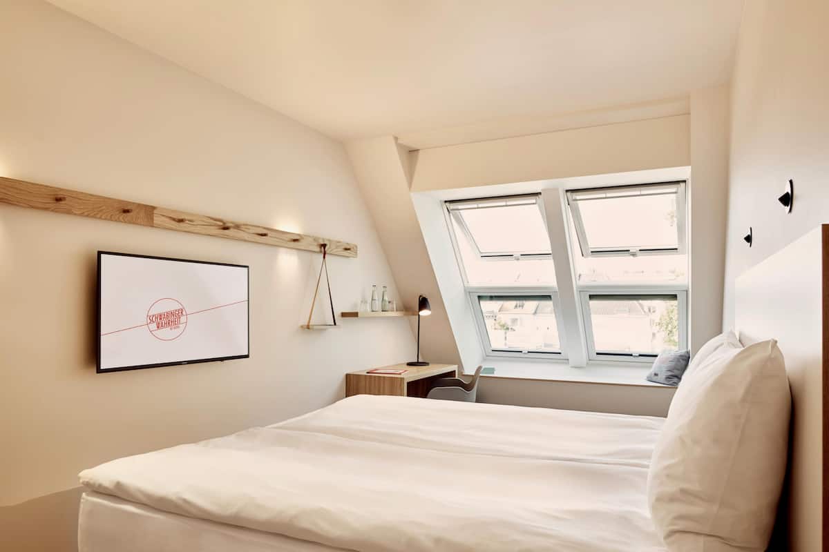 A bedroom with a bed, a desk, a chair, and a window with skylights.