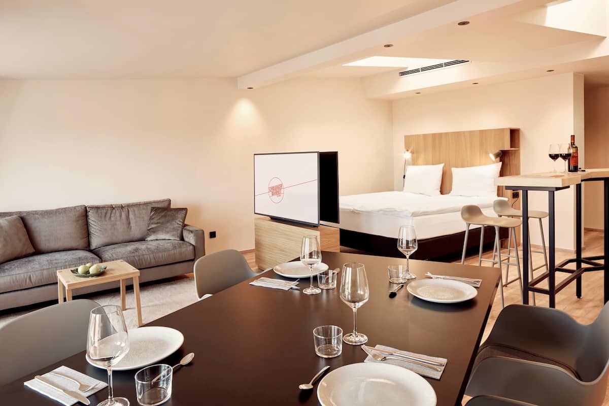 A modern hotel room with a dining area, a sofa, a bed, and a TV.