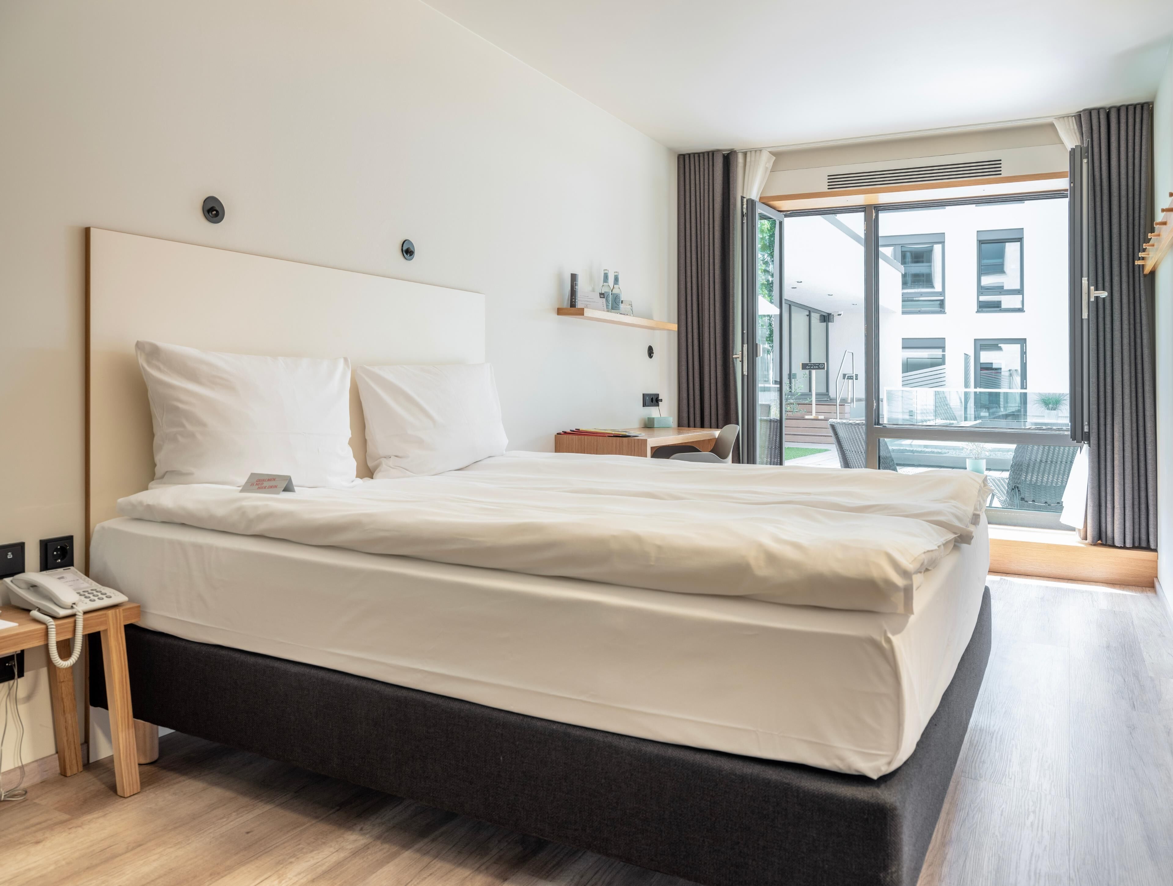 Una camera d'albergo moderna con un grande letto, un telefono sul comodino, una piccola scrivania e vista all'esterno.