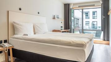 Una camera d'albergo moderna con un grande letto, un telefono sul comodino, una piccola scrivania e vista all'esterno.