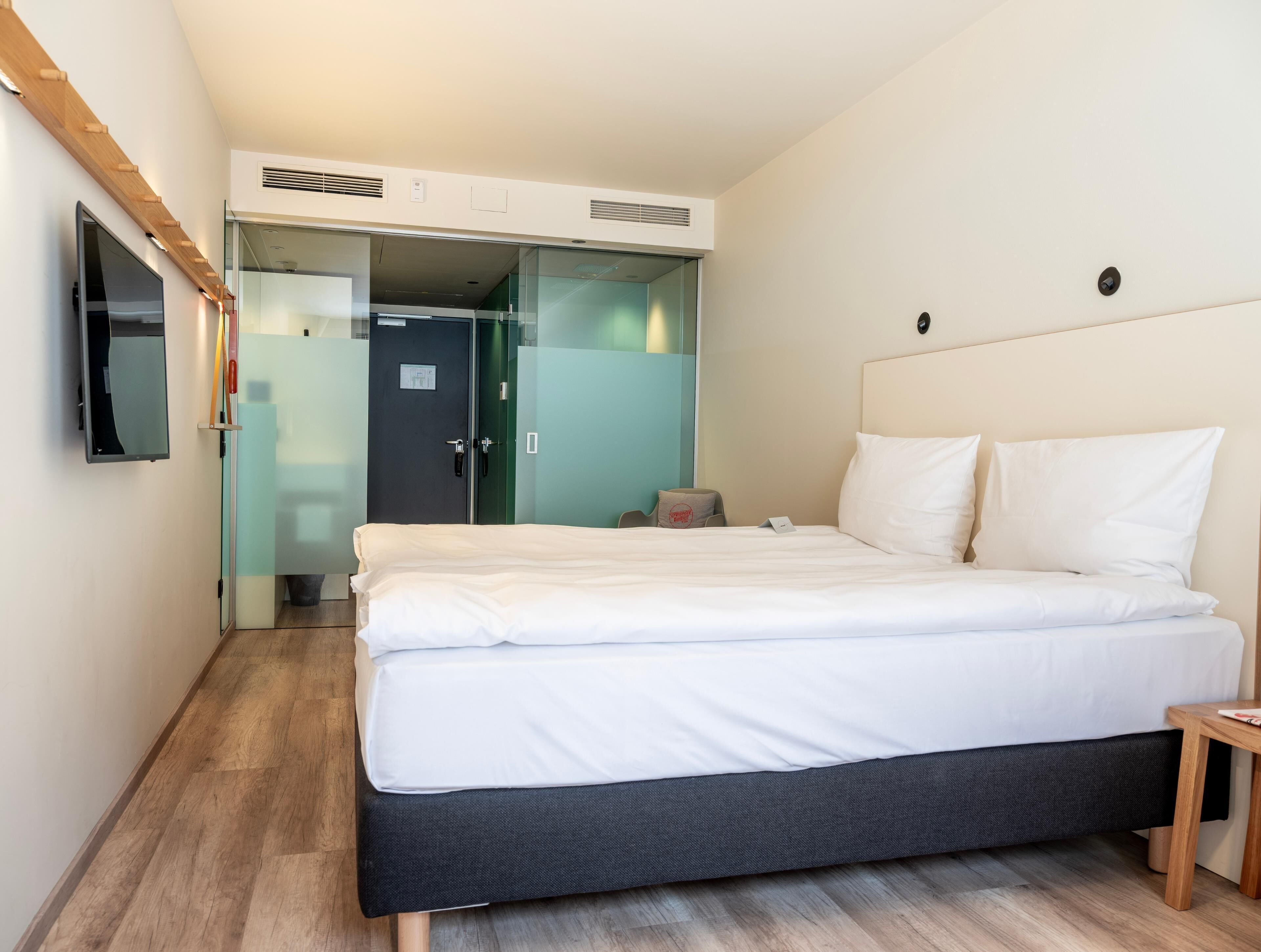 Une chambre d’hôtel moderne équipée d’un lit, d’une télévision, d’une armoire et d’une petite table.