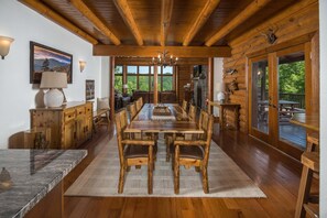 A log cabin interior with a large dining table, wooden chairs, a fireplace, and a view of the outdoors. - Private Mountaintop Retreat | Hot Tub, Sauna, Game Room & Views (Sugar Grove)