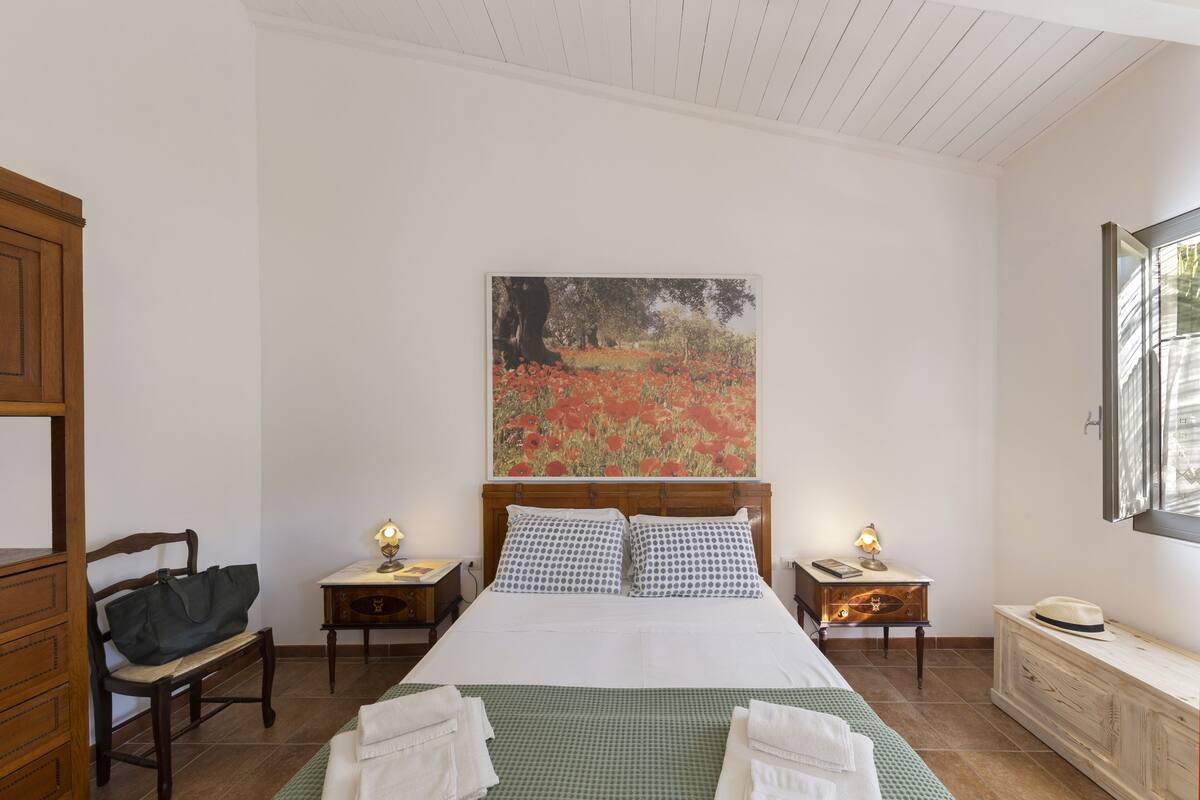 A bedroom with a large bed, two bedside tables, a wooden bench, a dresser, and a painting on the wall.
