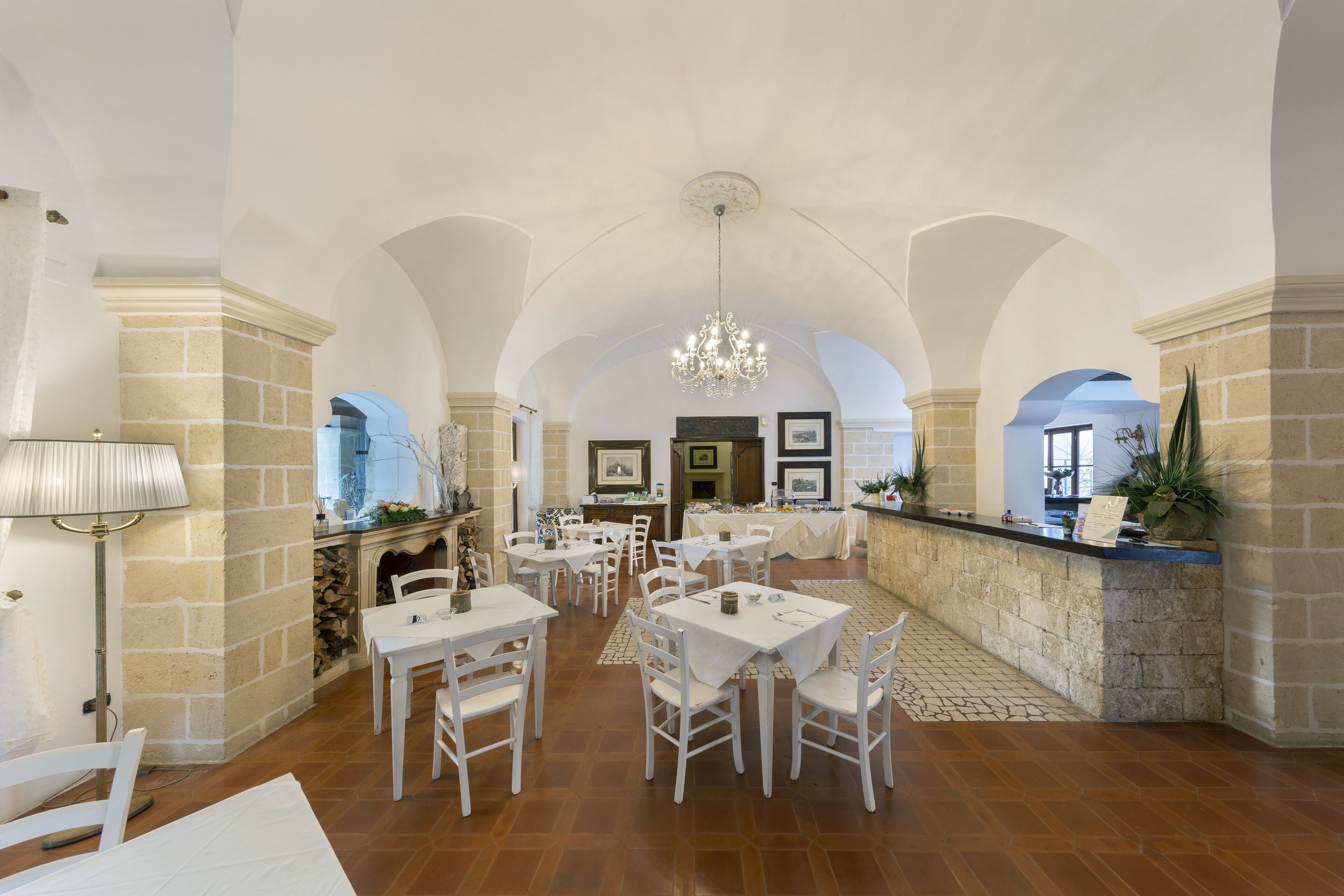 A spacious dining area with white tables and chairs, a stone fireplace, and a chandelier.