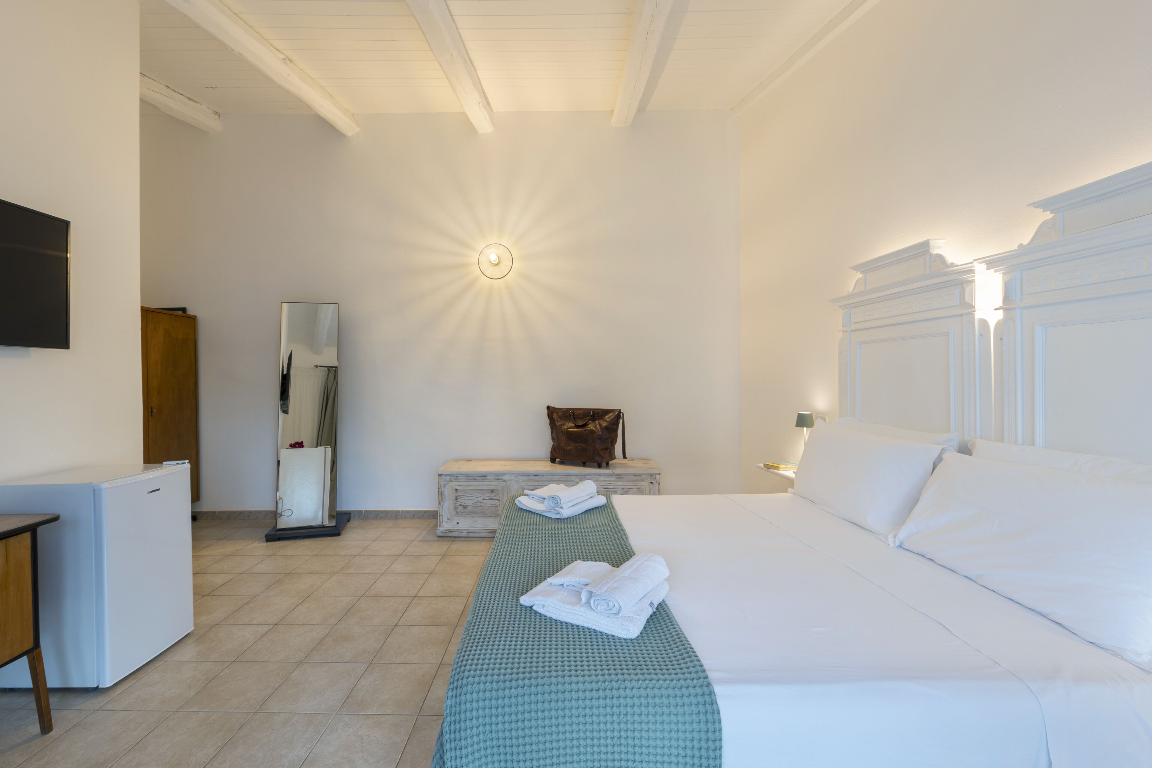 Une chambre d’hôtel équipée d’un lit, d’un bureau, d’un réfrigérateur, d’un miroir et d’un banc avec des serviettes.
