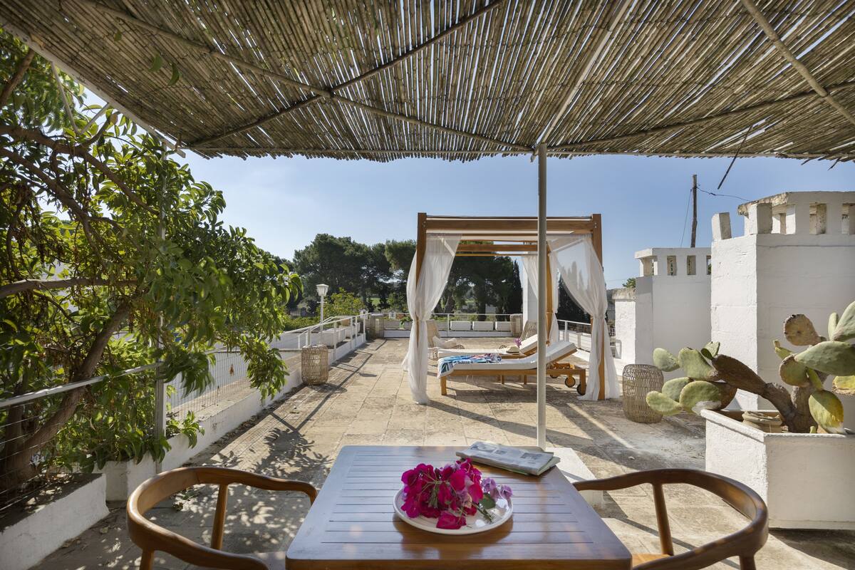 A covered outdoor seating area with a table, chairs, and a bed under a canopy.