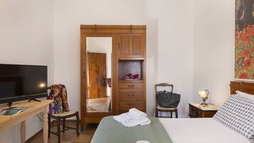 Una camera d'albergo con un letto, una TV, una scrivania con una sedia, un armadio e un quadro appeso al muro.