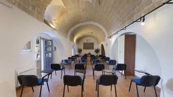 Un salón amplio con filas de sillas y mesas, techos abovedados y una pared de ladrillo rústico.