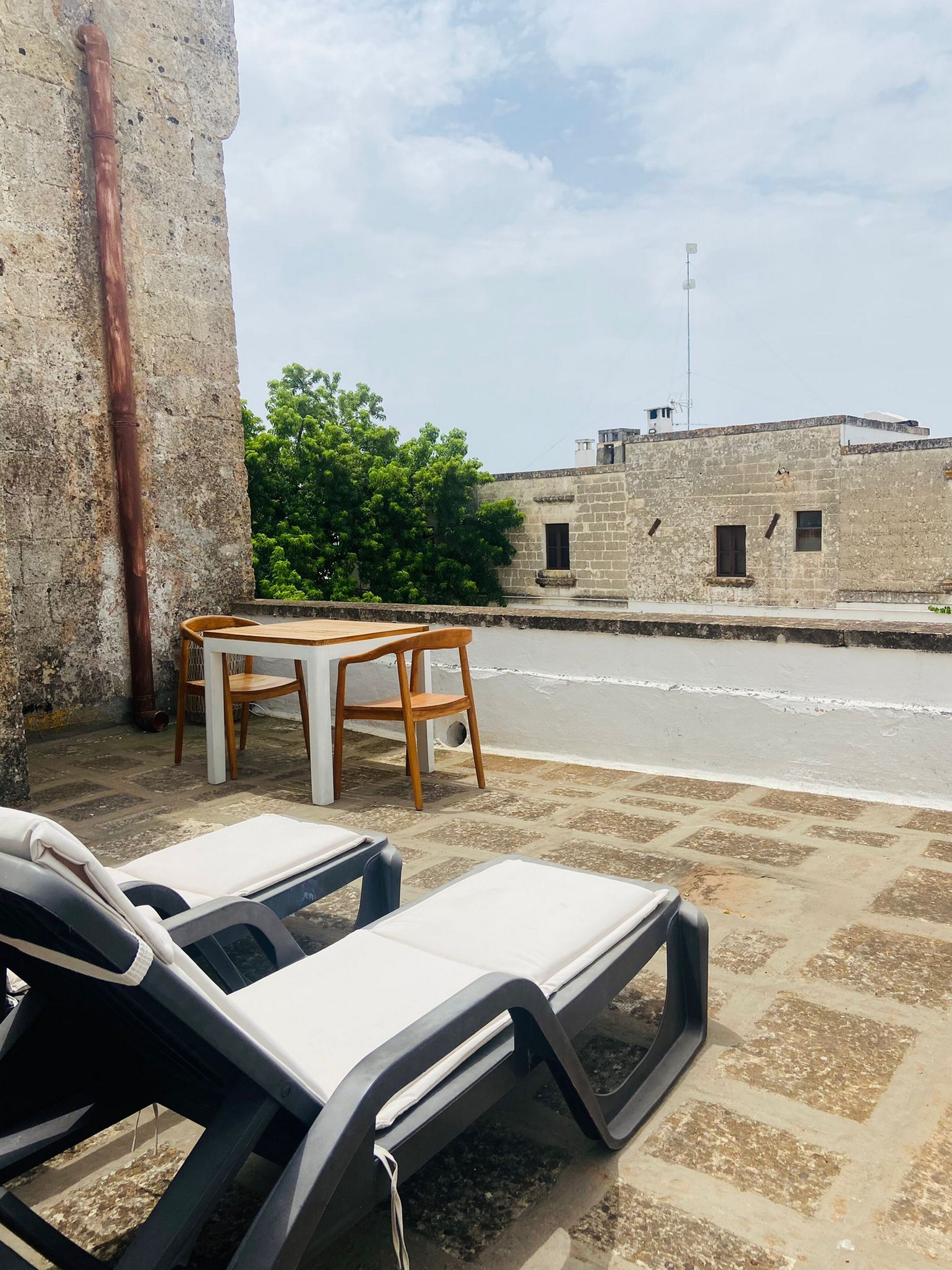 A balcony with two lounge chairs and a small table, overlooking a street with buildings and trees.