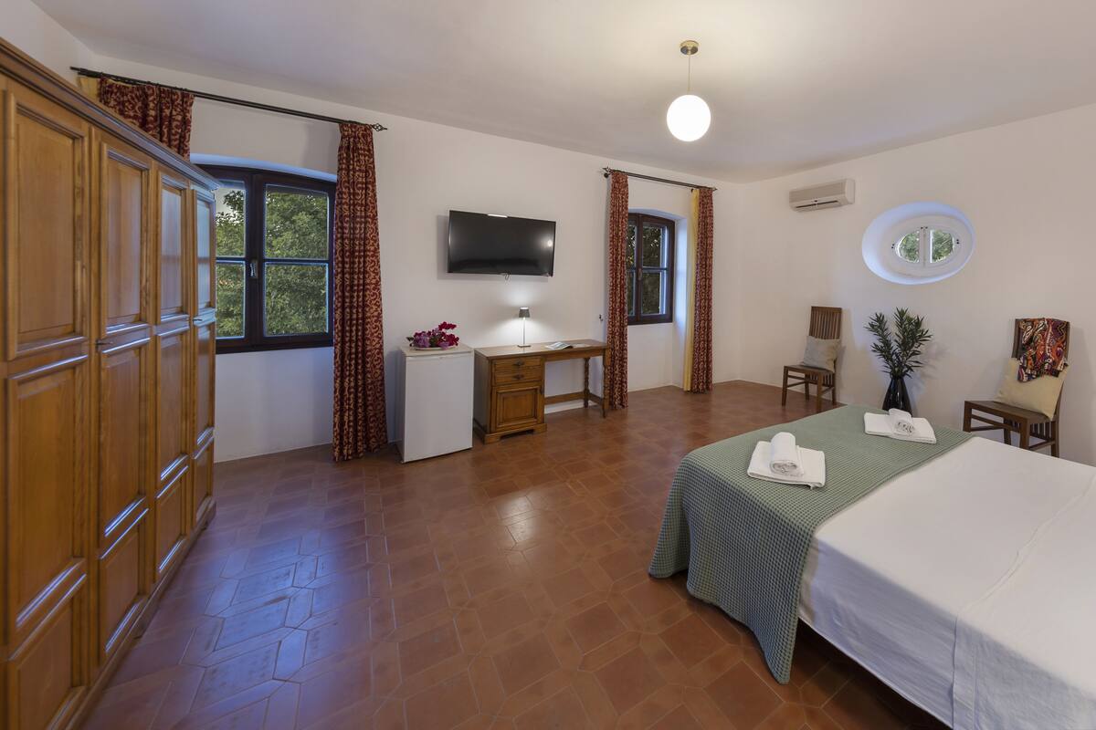 A hotel room with a bed, desk, TV, and large windows.