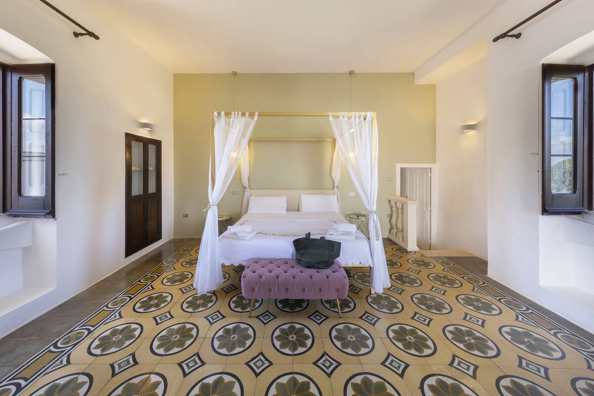 A bedroom with a four-poster bed, a small bench, and a patterned floor.