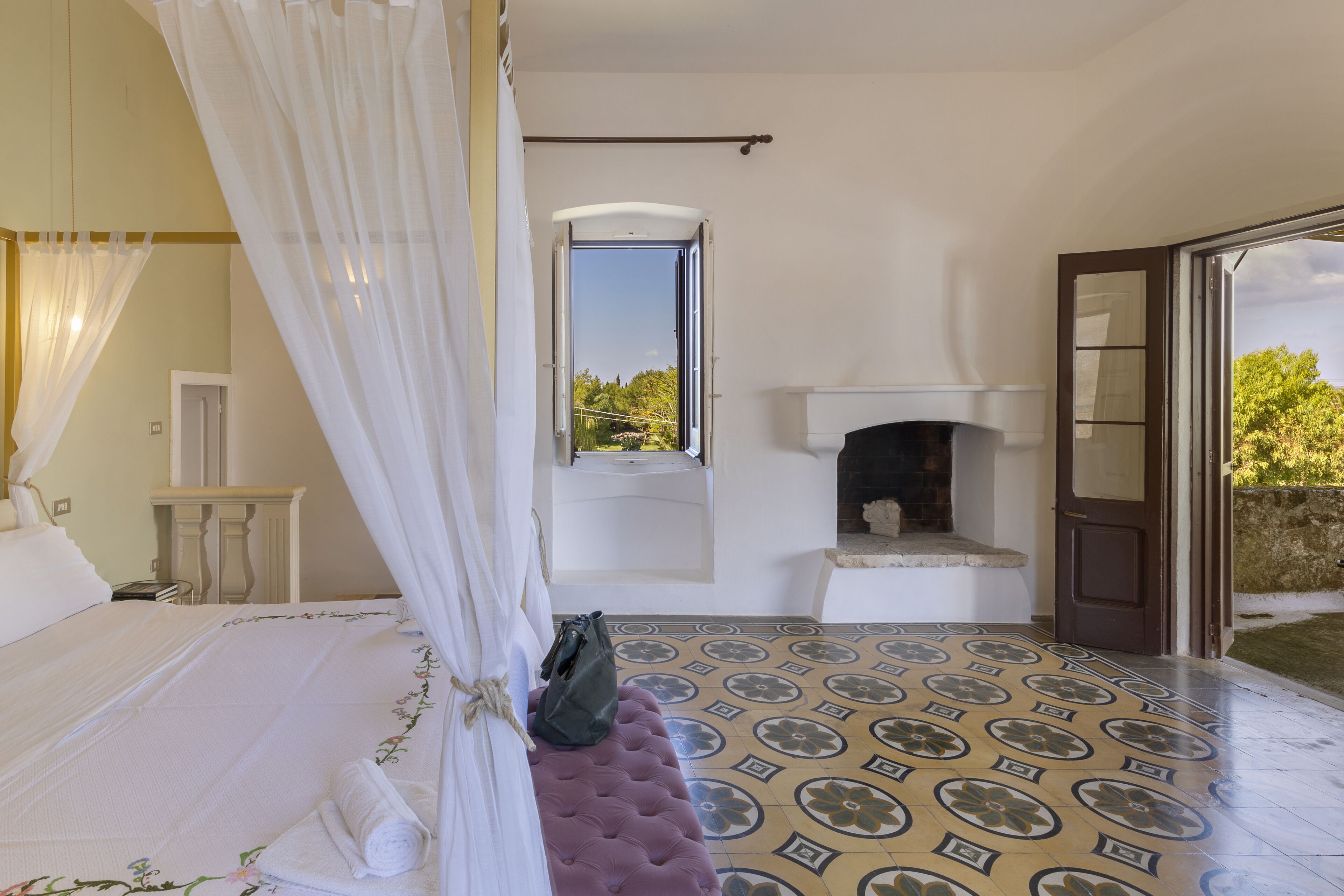 A bedroom with a bed, a window, a fireplace, and a view of the outdoors.