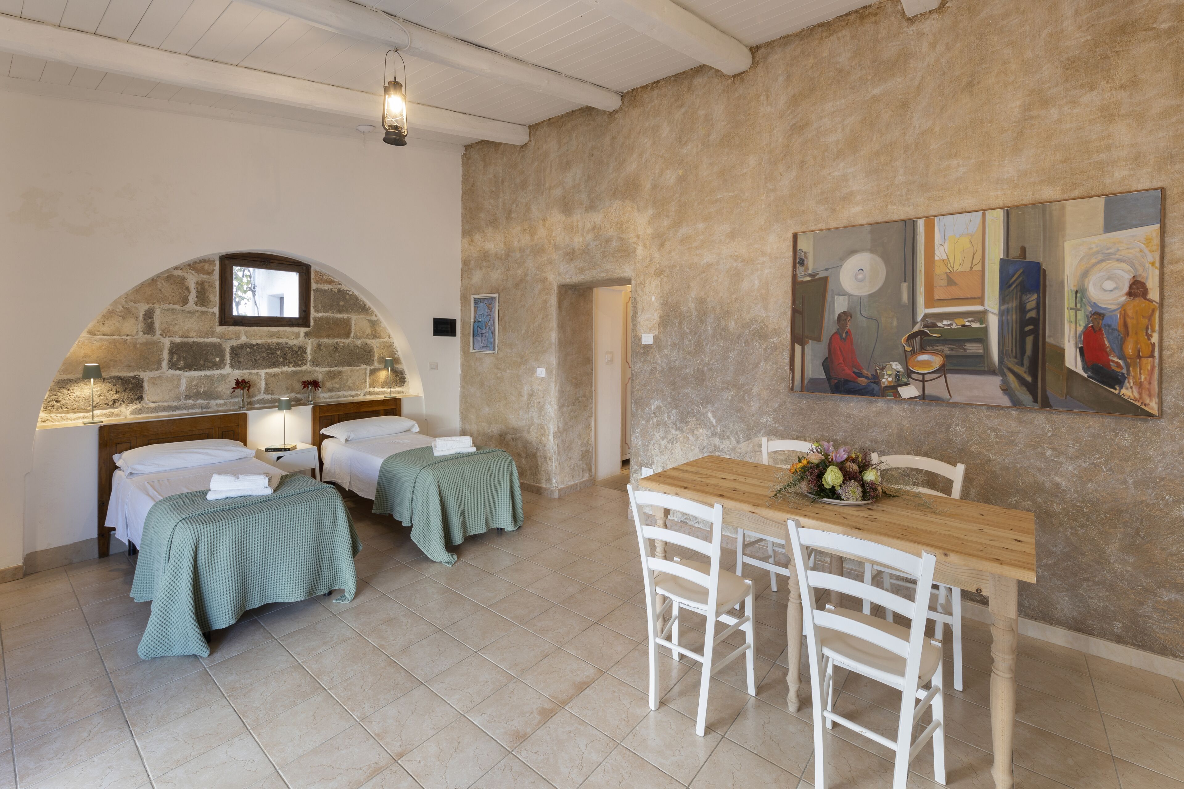 A room with two beds, a wooden table, and a painting on the wall.