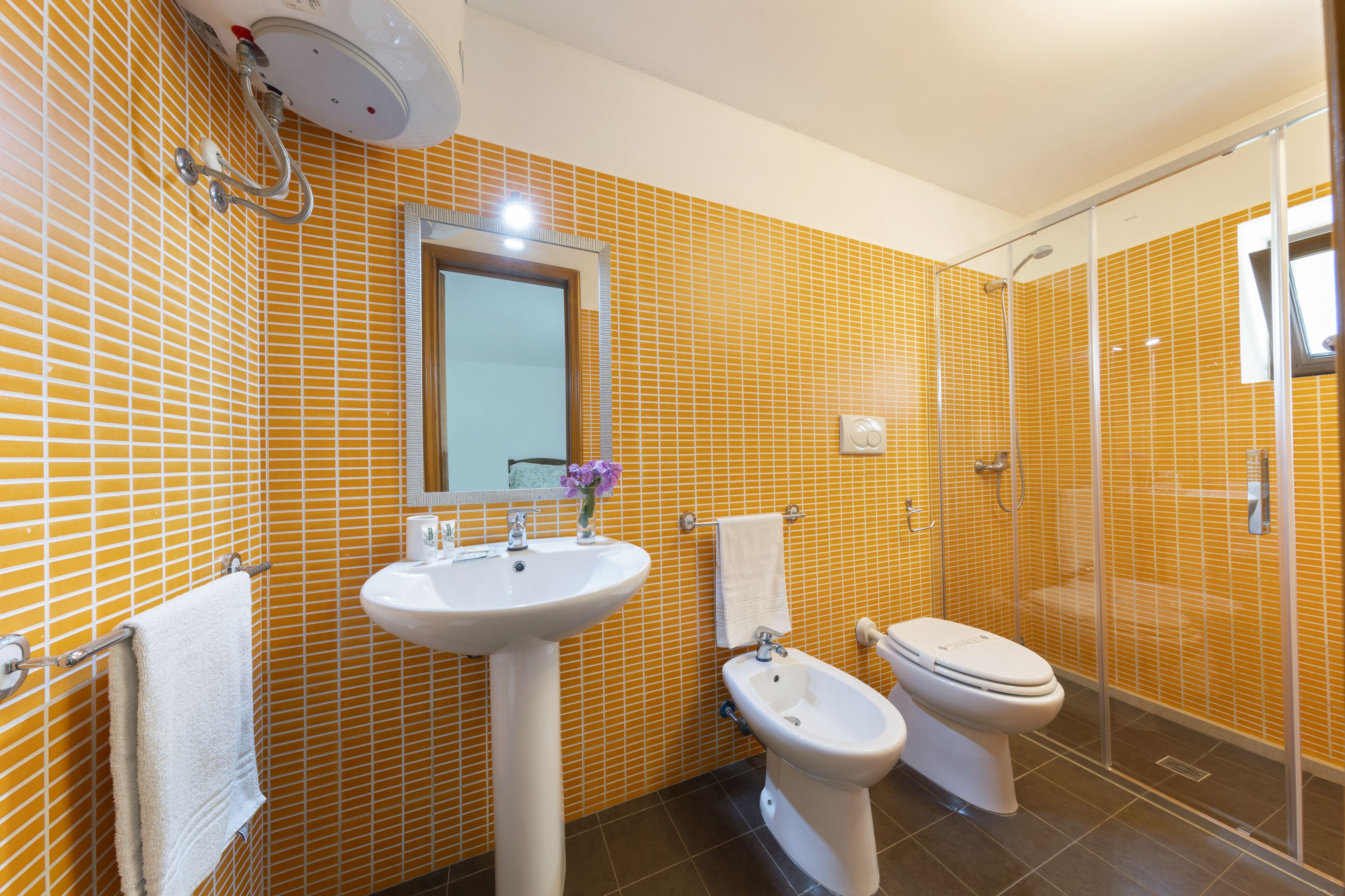 A bathroom with yellow tiled walls, a sink, a bidet, and a toilet.