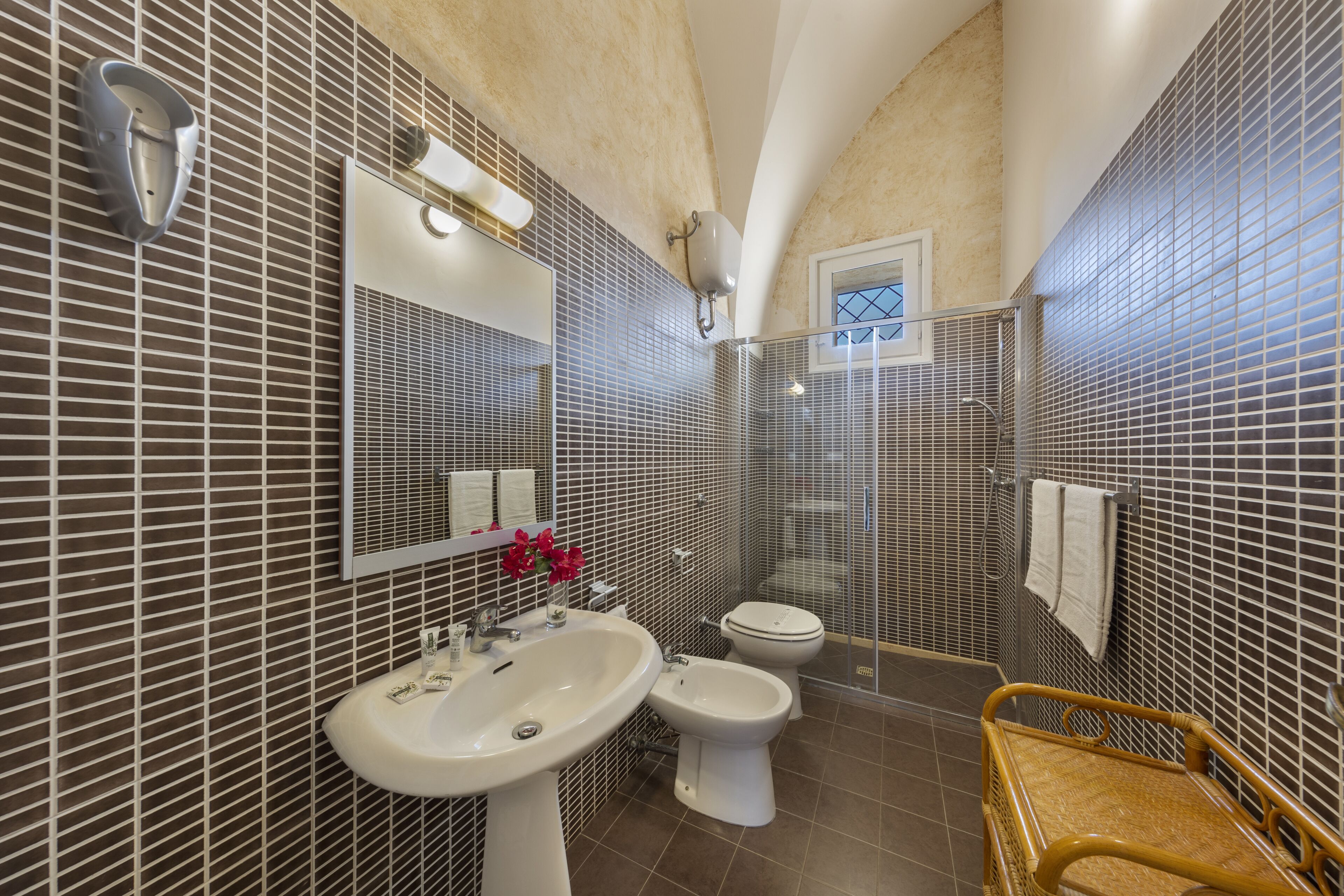 Un baño con lavamanos, bidé, inodoro y una silla de mimbre.