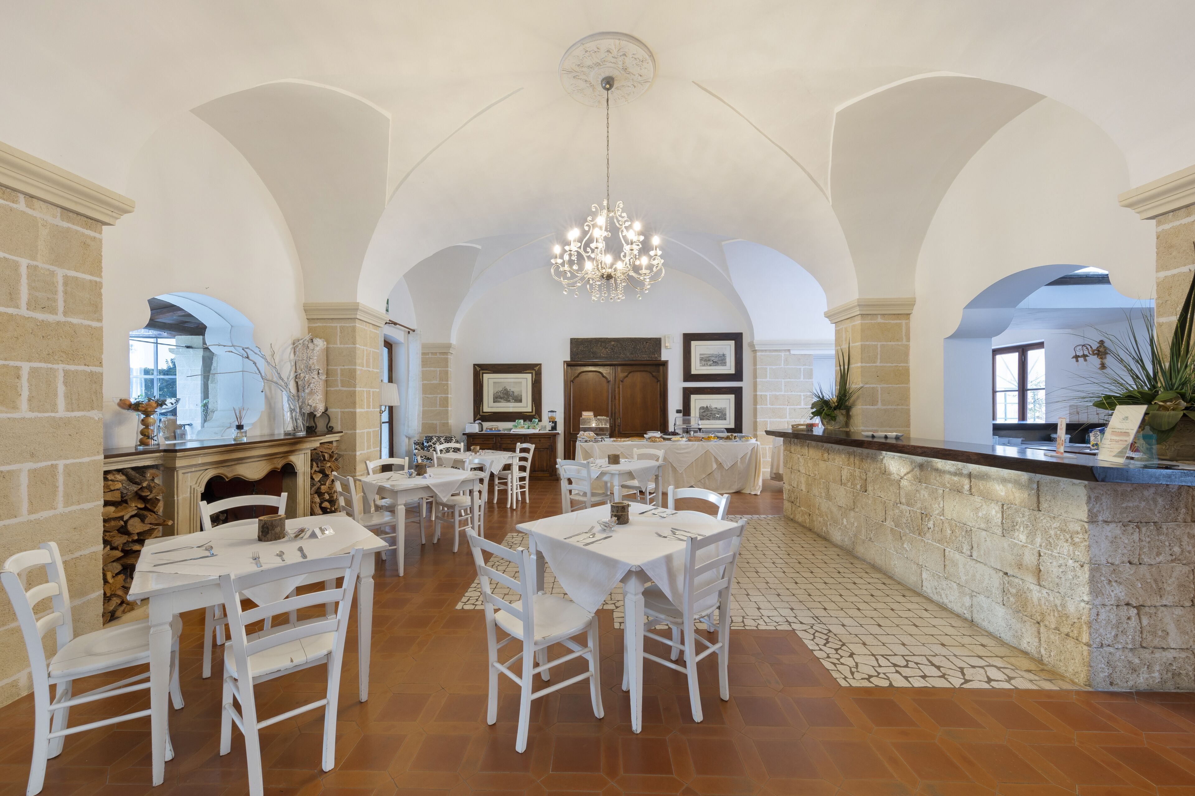 Une salle à manger spacieuse avec des tables et des chaises blanches, une cheminée en pierre et un lustre.