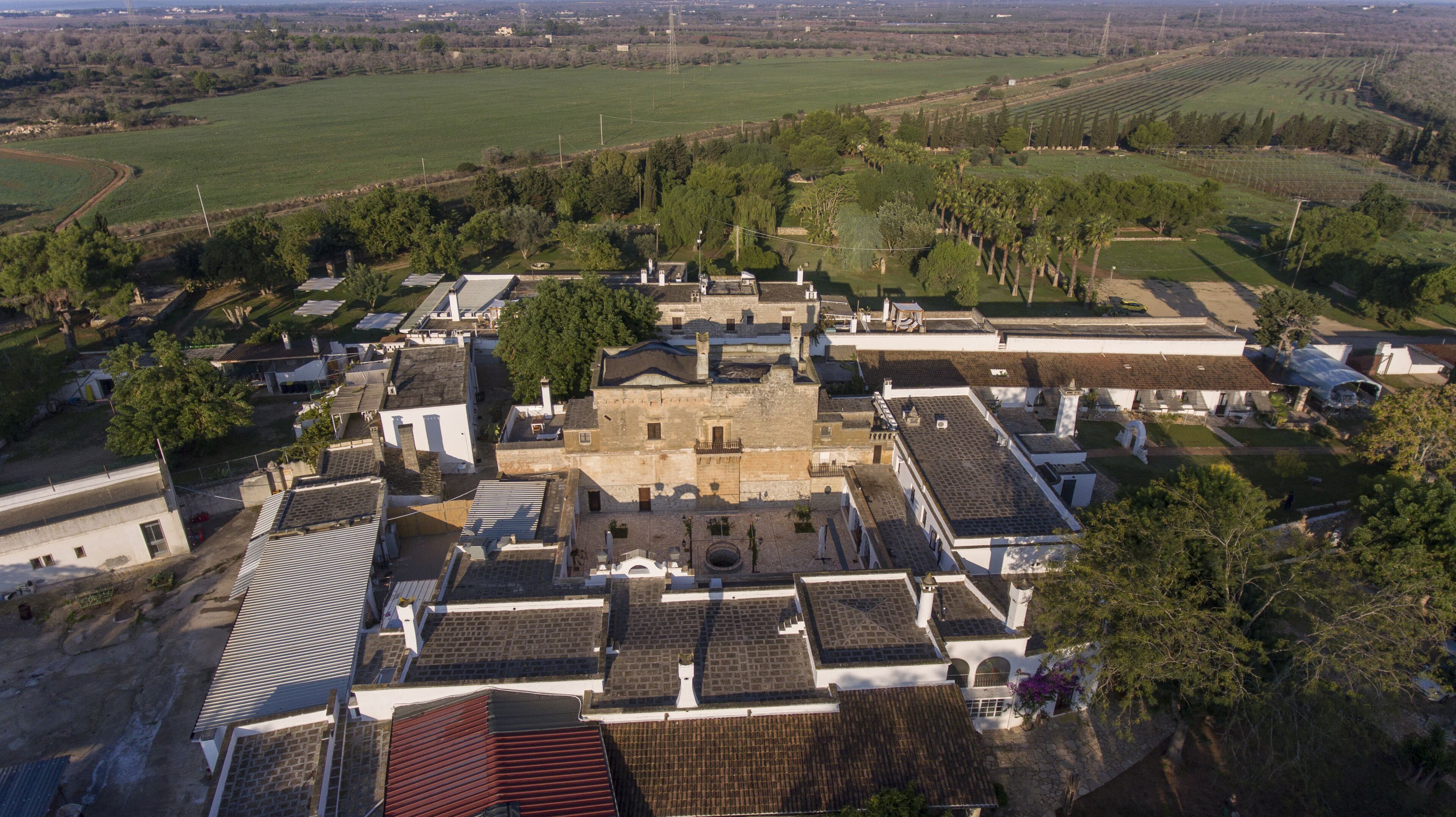 An aerial view of a historic town center with traditional buildings, cobblestone streets, and surrounding fields.