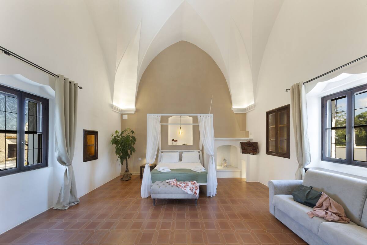 A spacious bedroom with a large bed, a sitting area, and a high arched ceiling.