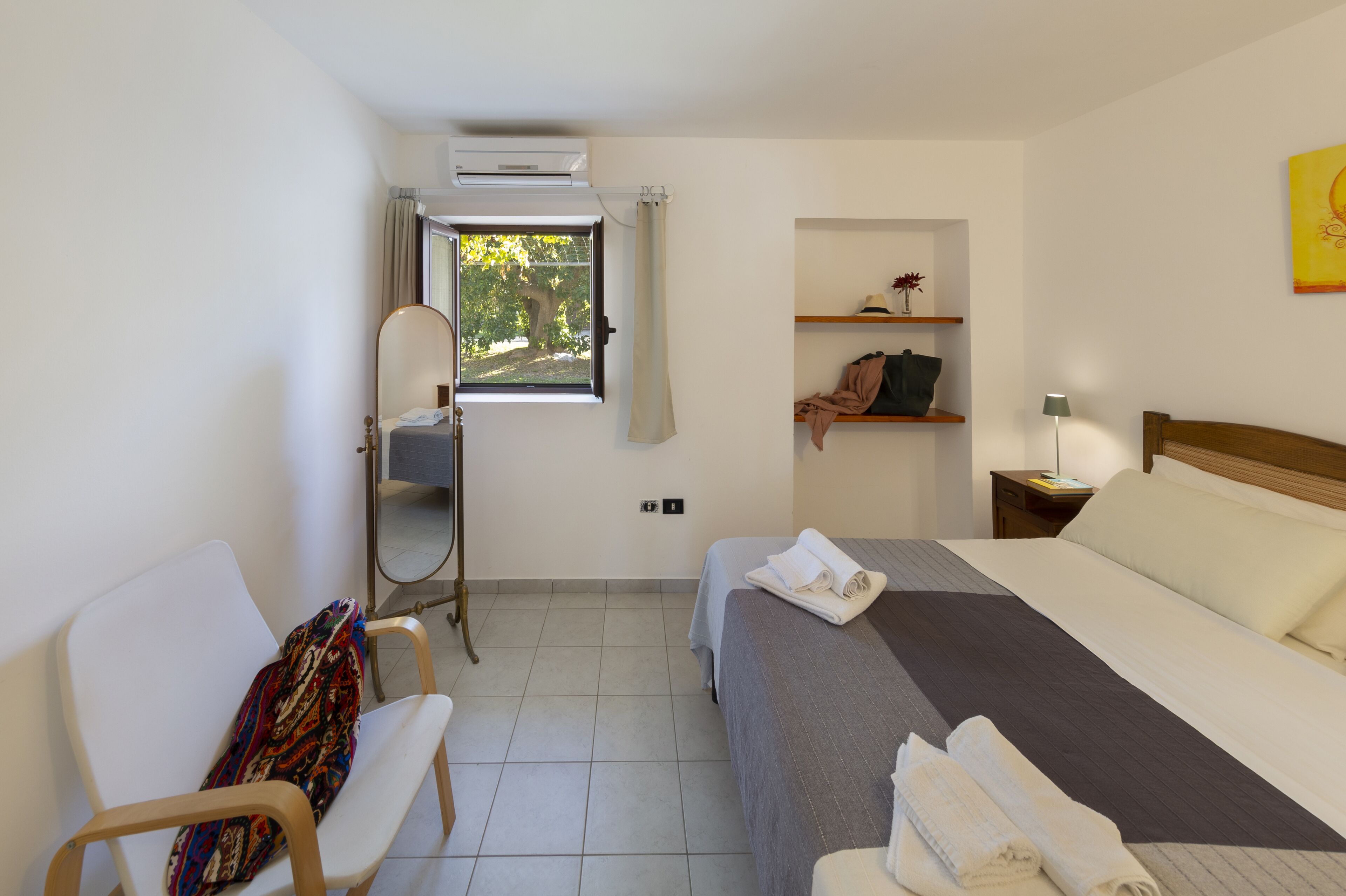 Une chambre d’hôtel comprenant un lit, une chaise, un bureau, une étagère avec des objets décoratifs et une fenêtre avec des rideaux.