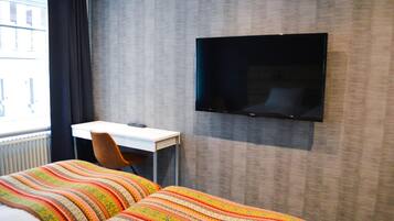 Habitación de hotel con dos camas, un escritorio, una silla y un televisor de pantalla plana montado en la pared.