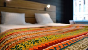 A bed with a colorful blanket, a wooden headboard, and a window with a view. - Hotell Stortorget (Östersund)