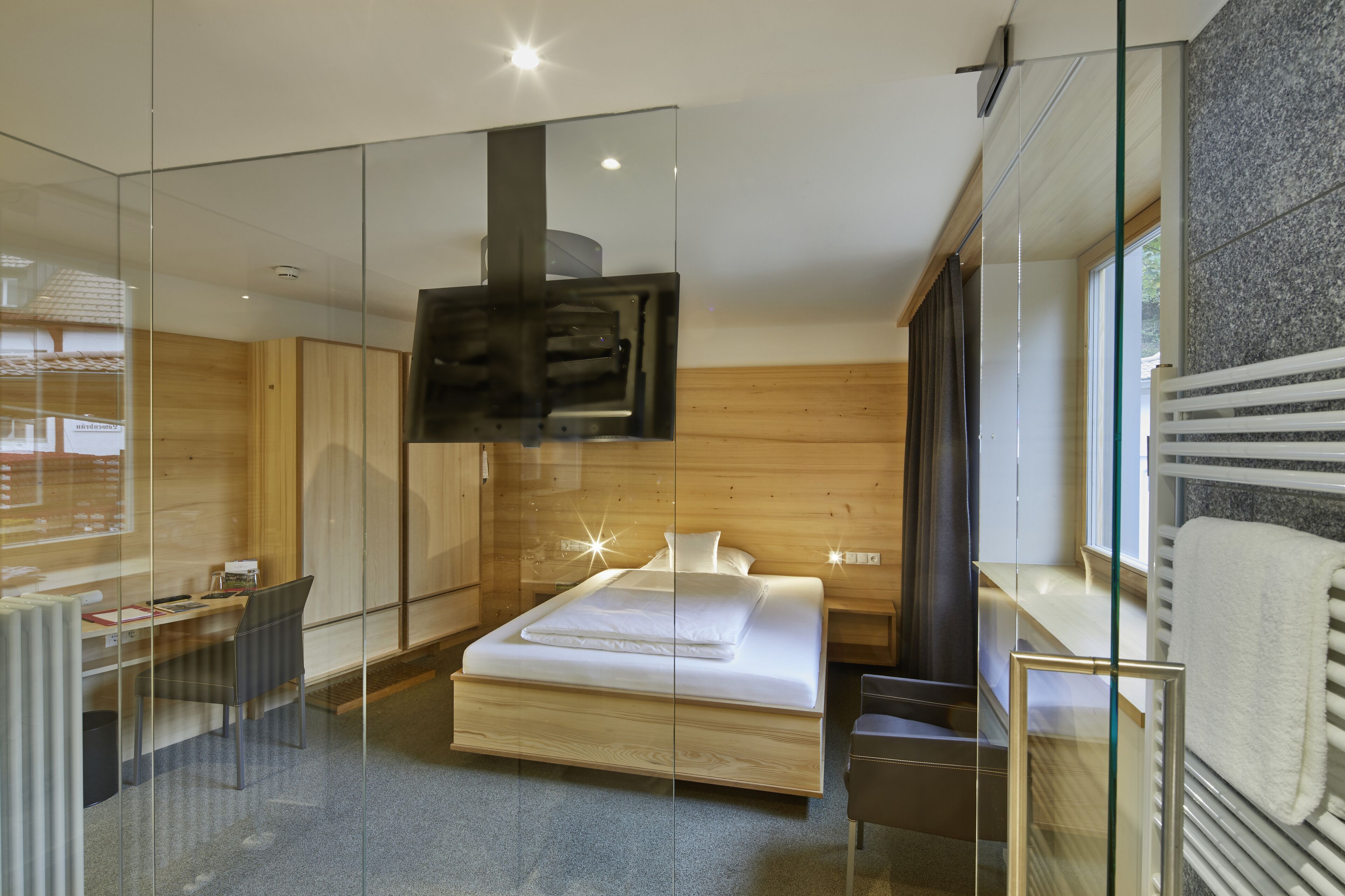 Un dormitorio moderno con un separador de vidrio, cama, escritorio y televisor.