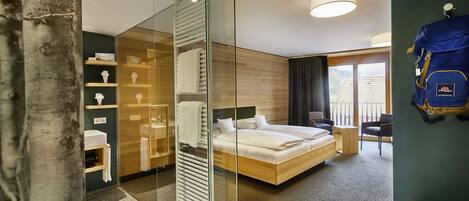 A modern hotel room with a glass partition, a wooden bed, a small desk, and a view of the outside.