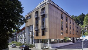 Un edificio moderno de varios pisos con balcones, ventanas amplias y una zona de estacionamiento.
