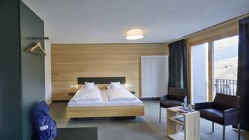 A hotel room with a bed, two chairs, a small table, a radiator, and a view of the outside.