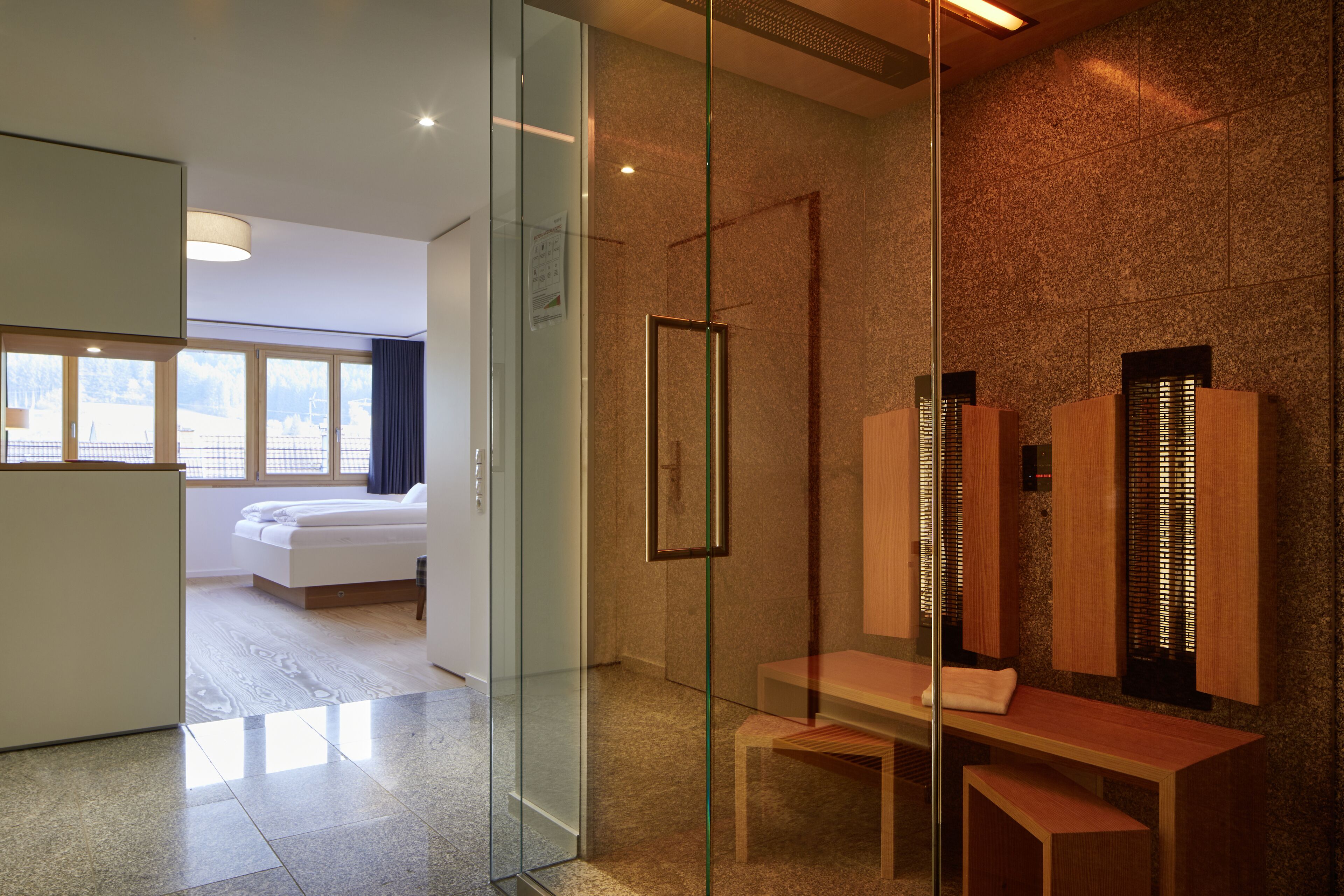 Une chambre d’hôtel moderne avec une cloison en verre, un banc en bois et un grand miroir.