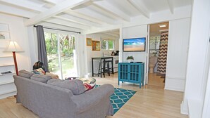 Una sala de estar moderna con un sofá gris, un comedor con una cocina al fondo, y un televisor montado en la pared.