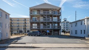 A multi-story residential building with balconies, a staircase leading to the entrance, and a parked car in front.