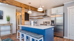 A modern kitchen with a central island, bar stools, stainless steel appliances, and a wooden ceiling.