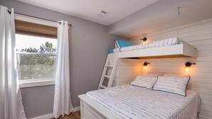 A bedroom with a bunk bed, a window with curtains, a wooden floor, and wall-mounted lights.
