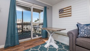 A room with a sliding glass door, a wooden table, a gray sofa, and a patterned pillow.