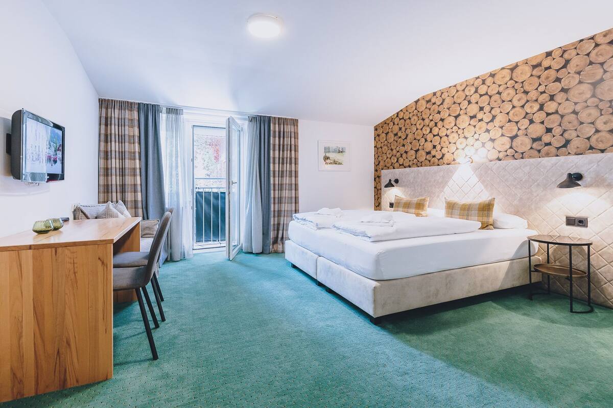 Une chambre d’hôtel équipée d’un lit, d’un bureau, d’une chaise, d’une télévision et d’un balcon avec des rideaux.