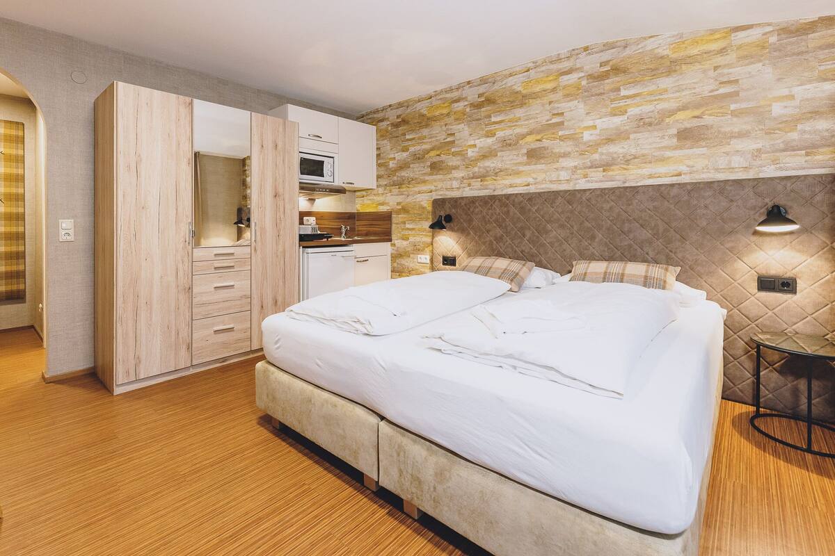 Une chambre avec un grand lit, une armoire en bois et un mur décoré d’un motif imitant la pierre.