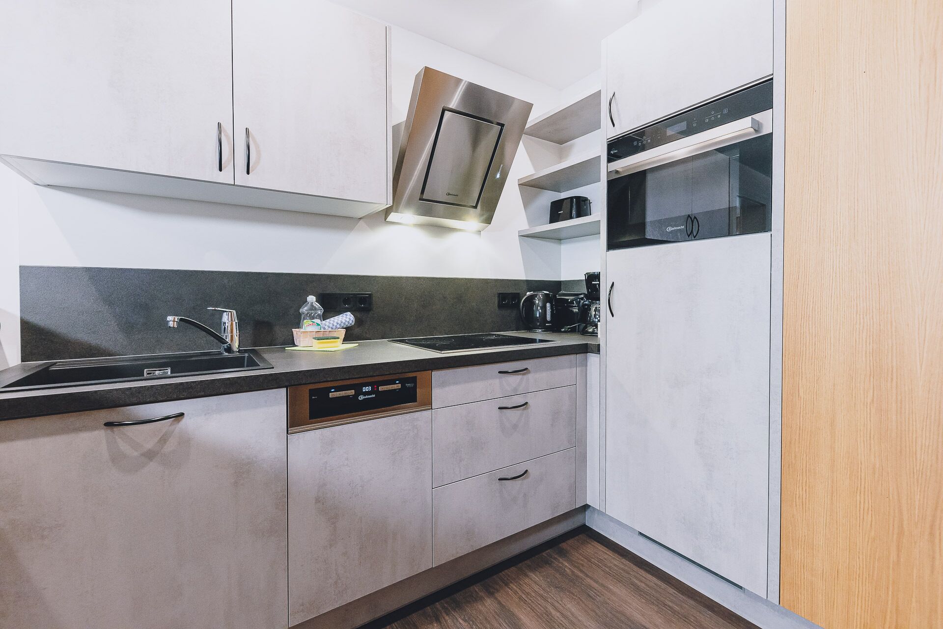 A modern kitchen with a stainless steel range hood, a built-in oven, and a dishwasher.