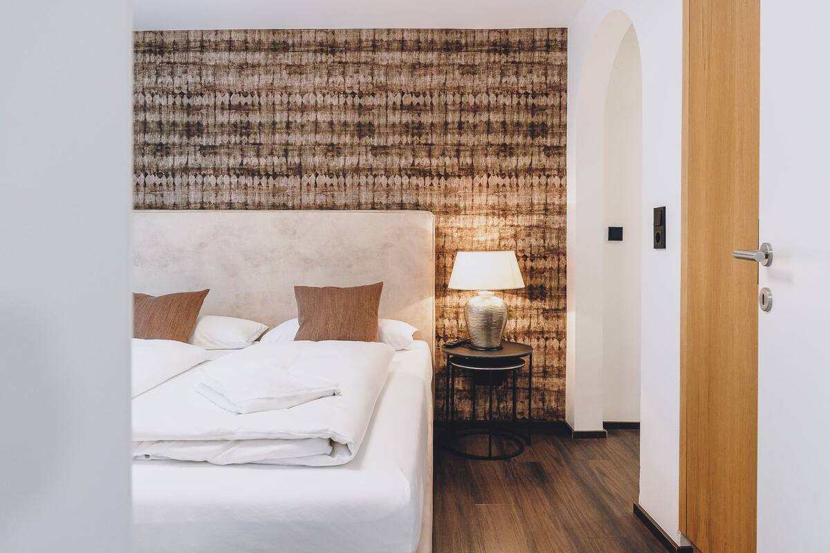 Un lit bien fait, avec des oreillers, une lampe de chevet et un mur à motifs en arrière-plan.
