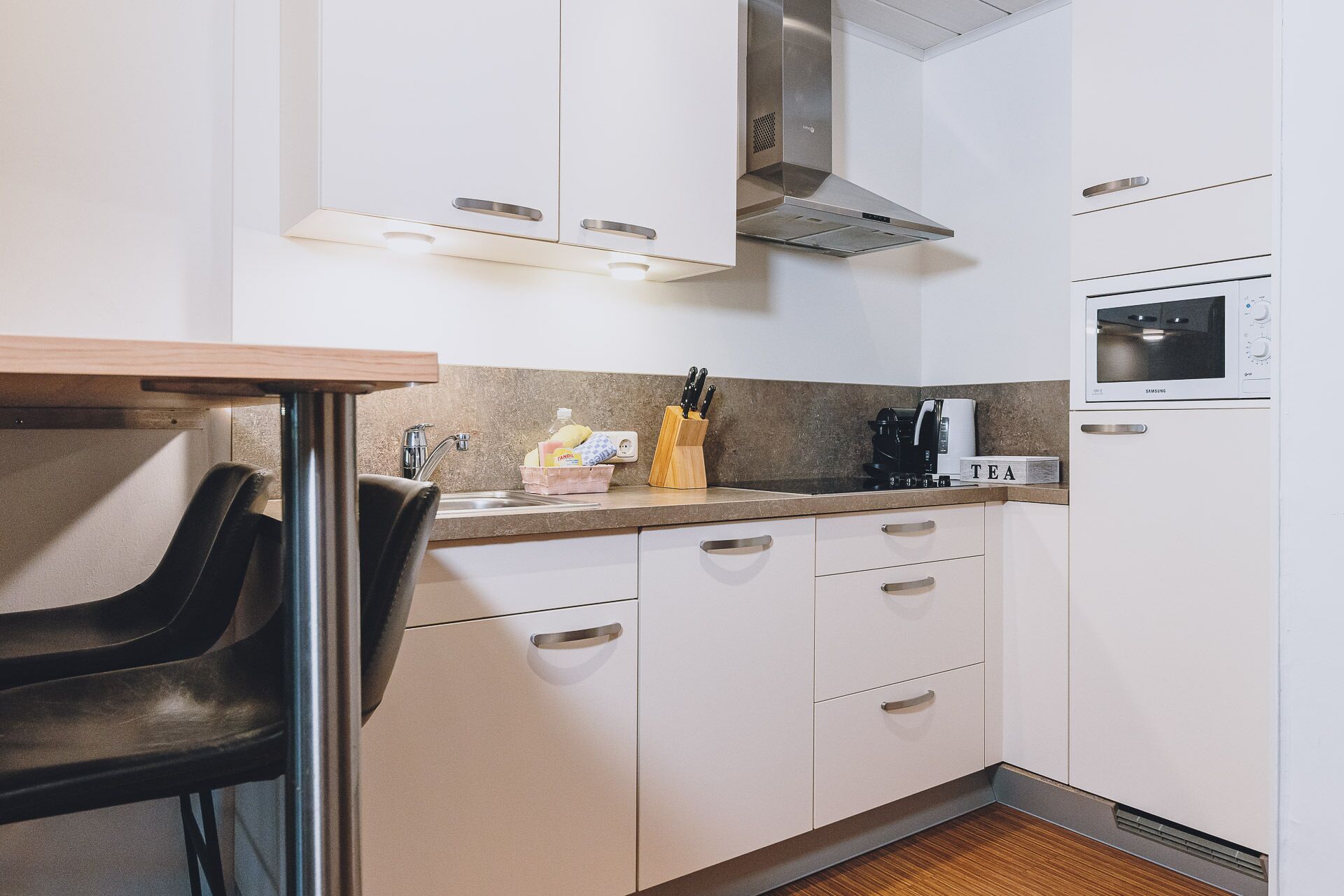 A compact kitchen with white cabinets, a stainless steel sink, a microwave, and a coffee maker.
